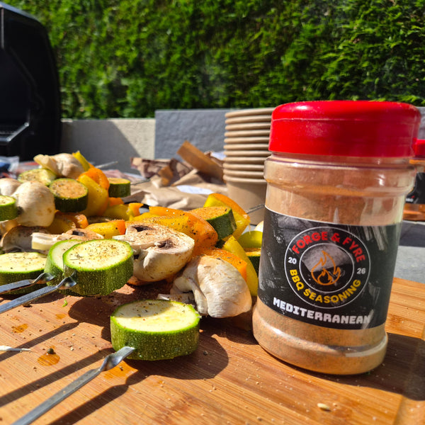 Skewers of courgette, mushroom and pepper seasoned with Forge & Fyre Mediterranean rub, resting on a wooden board beside the jar