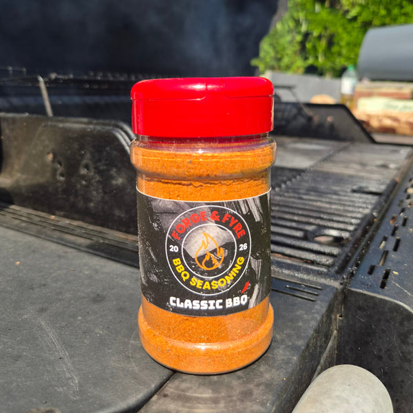 A bottle of Classic BBQ spice rub by Forge & Fyre BBQ Seasoning sits on the edge of a black grill outdoors