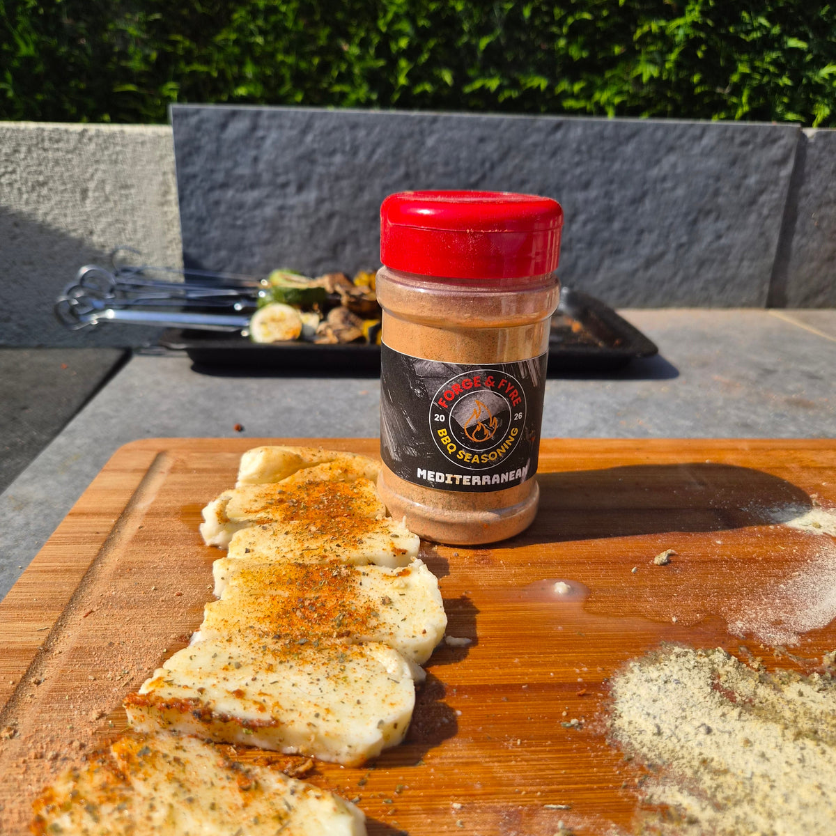 Slices of halloumi dusted with Forge & Fyre Mediterranean rub on a wooden board, with the jar of seasoning behind