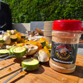 Skewers of courgette, mushroom and pepper seasoned with Forge & Fyre Mediterranean rub, resting on a wooden board beside the jar