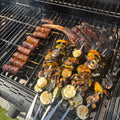 Vegetable skewers and a tomahawk steak cooking over the bars of a black barbecue grill